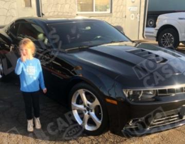 girl standing next to a Camaro giving a thumbs up